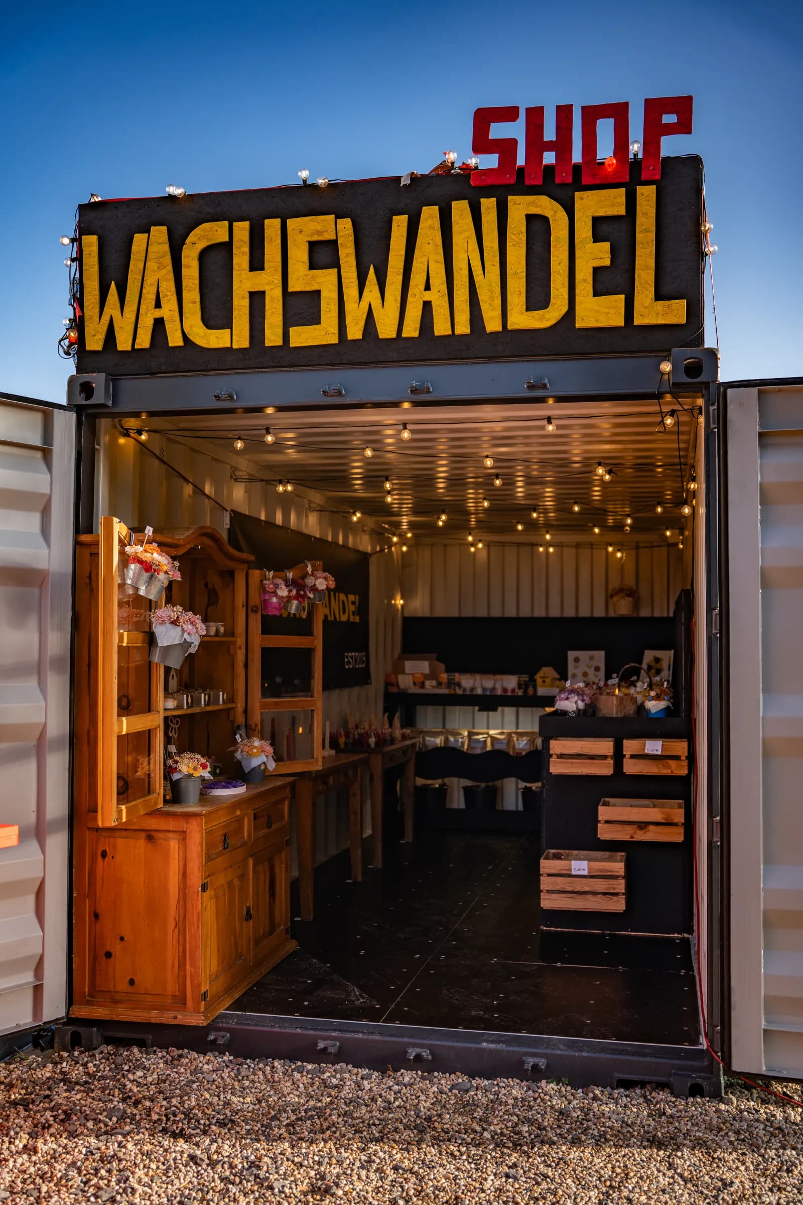 Der Wachswandel-Shop in Weilerswist: ein Container mit gelbem Schriftzug, die Türen offen, drinnen Lichterketten und Regale mit Kerzen